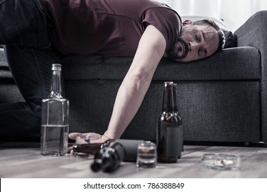 After drinking. Drunk bearded adult man lying on the sofa and sleeping after drinking lots of alcohol - Shutterstock ID 786388849