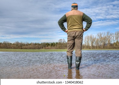 After an extremely heavy rainfall in Germany a farmer stands with his rubber boots in the middle of a huge puddler and looks at his flooded meadow.