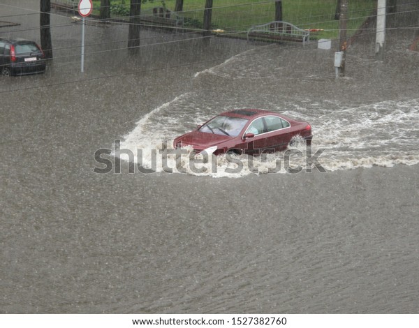 After heavy rain\
there is a flood on the city roads. The car hardly rides in the\
water to the level of the\
hood