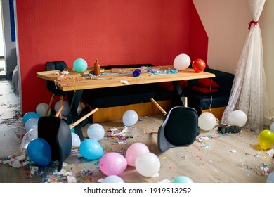After Party Chaos, Messy In Livving Room At Home, Table With Pizza And Champagne Glasses Covered With Confetti And Ballons, Chair On The Floor At Morning After Party Celebration.
