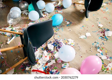 After Party Chaos, Messy In Livving Room At Home, Table With Pizza And Champagne Glasses Covered With Confetti And Ballons, Chair On The Floor At Morning After Party Celebration.
