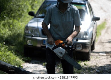 After Severe Weather Works of Maintenance - Senior Man Cutting a Fallen Tree over a Road with a Chainsaw  - Powered by Shutterstock