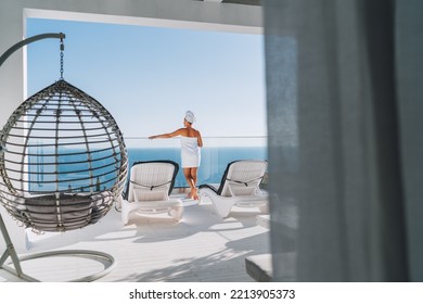 After Shower Beautiful Woman With Hair And Body Towel Wrap Standing On Open House Terrace With Sunbeds, Hanging Chair Enjoying Seascape And Blue Clean Sky. Body Care, Beuty And Home Lifestyle Concept