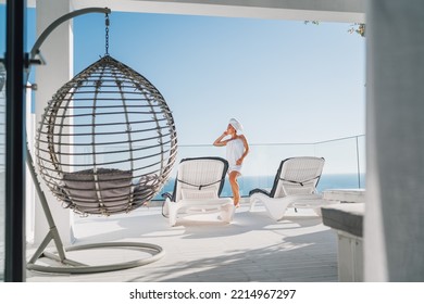 After Shower Beautiful Woman With Hair And Body Towel Wrap Standing On Open House Terrace With Sunbeds, Hanging Chair Enjoying Seascape And Blue Clean Sky. Body Care, Beuty And Home Lifestyle Concept