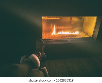 After Ski Resort Woman Wearing Winter Boots Sitting By Gas Bio Ethanol Fireplace At Night Cozy Fire Place With Flames Glowing In The Dark.