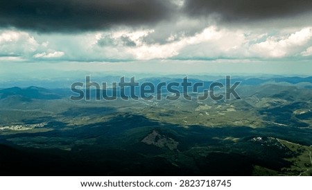 After a squall the uplands glisten with subtle light and texture. Dark ridges step away into layered blue distance while valleys shine and the sky holds a heavy ceiling of cloud