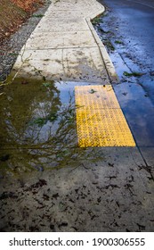 After The Storm, Floodwater And Storm Debris On A Sidewalk Disabled Curb Ramp On A Sunny Day
