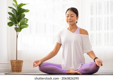 After waking up at home, a woman does morning yoga, sitting in Easy position, Sukhasana posture, and meditating.