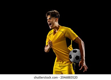 After winning game. Happy proud male football player in yellow uniform isolated over dark background. Successful competition. Concept of action, speed, energy, sport, competition and ad.