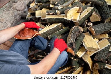 After work. A man in jeans sits in the yard on a stone fence. Under it lies a large pile of firewood. leather hat in hand