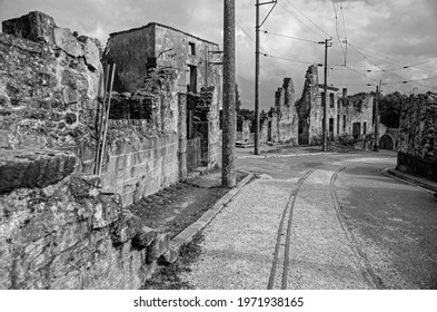 Aftermath Of War Monochrome, War Memorial In France With Tram Lines In The Road Leading Towards Derelict Buildings.  Deserted Village Left As A Reminder To Others.