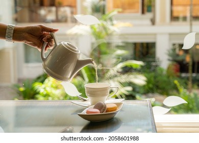 Afternoon Tea Time A Woman's Hand Pouring Tea Into A White Ceramic Mug. There Are Macarons To Eat Together. 