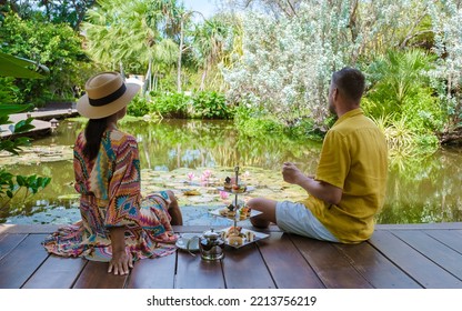 Afternoon Tea At A Water Pond, High Tea In A Tropical Garden In Thailand. Couple Of Men And Women Having High Tea In A Tropical Garden