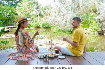 Afternoon Tea At A Water Pond, High Tea In A Tropical Garden In Thailand. Couple Of Men And Women Having High Tea In A Tropical Garden