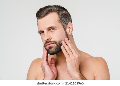 Aftershave cosmetics. Caucasian young naked shirtless man preparing for shaving with razor touching his beard isolated in white background