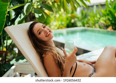 Against the backdrop of the pool lies on the shizlong woman with a glass of gently smiling. High quality photo