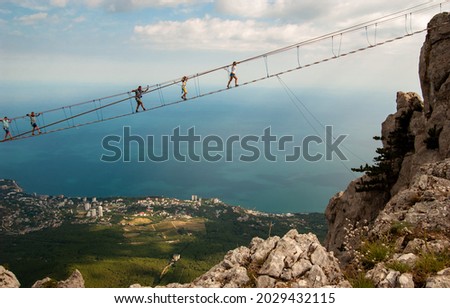 Against the background of the city and the blue sea at a great height, tourists walk over the abyss on rope bridges. Experience the thrill. Mount Aypetri, Yalta, Crimea.