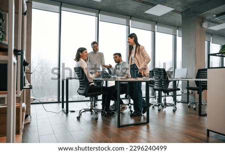 Against big windows by the table. Four people are working in the office together.