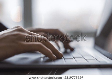 Against a blurred office background, the image captures a woman's hands typing on a sleek laptop keyboard