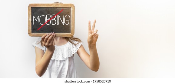 AGAINST MOBBING - Young girl with school blackboard with the word MOBBING shows peace sign ( victory hand symbol ) with her hand and fingers, isolated on white background banner panorama - Shutterstock ID 1958520910