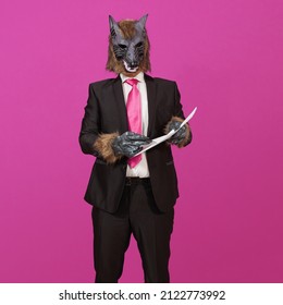 Against a pink background is a man dressed in a black suit with a jacket, white shirt and tie, wearing a werewolf mask, holding a document and pen offering to sign it.