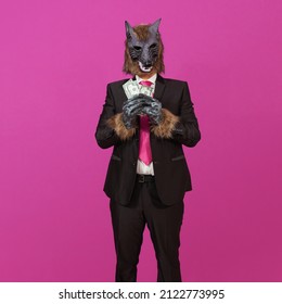 Against a pink background is a man dressed in a black suit with jacket, a white shirt and tie, wearing a werewolf mask, holding three 50 US dollar bills.