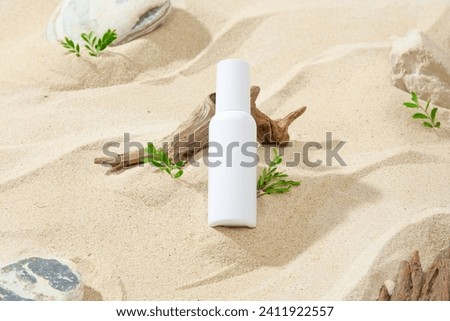 Against the sand background with gray and beige stones, dry twig and grass, a white cosmetic tube displayed. Mockup scene for advertising, summer beach concept