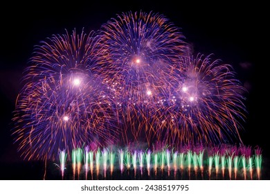 Against the velvety night sky, bursts of brilliant fireworks ignite, casting a mesmerizing spectacle of color and light. Each explosion sends cascades of shimmering sparks in all directions.