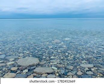 Agate stones beach of Lake Huron with crystal clear water, broken tree trunk and cloudy sky - Cape Chin, Bruce Peninsula ON