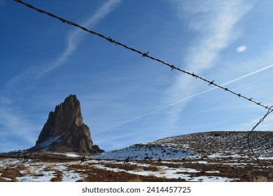 Agathla Peak also called El Capitan behind chain link fence at Highway 163 (Monument Valley Scenic Road) in Arizona near Kayenta on a sunny day in January