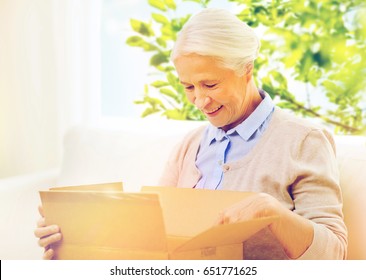 Age, Delivery, Mail, Shipping And People Concept - Happy Smiling Senior Woman Looking Into Open Parcel Box At Home