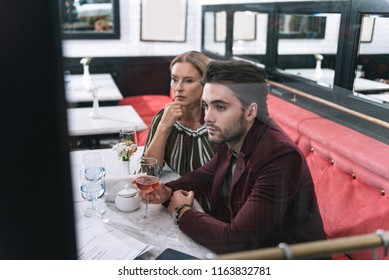 Age Difference. Anxious Pensive Woman Touching Face And Man Carrying Glass Of Wine