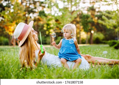 Age mother with a small daughter lying on the lawn in the park and blowing soap bubbles. Summer, vacation, maternity leave, childhood
