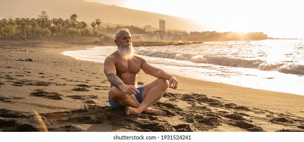 Age is only a number. In a healthy body, healthy mind. Senior man with white stylish beard meditating on the beach, lotus position. Summer vacation workout. Healthy lifestyle on a retirement concept. - Powered by Shutterstock