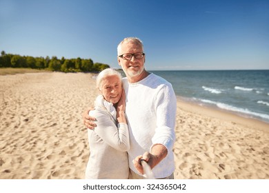 age, travel, tourism, technology and people concept - happy senior couple taking picture with smartphone selfie stick on summer beach - Powered by Shutterstock