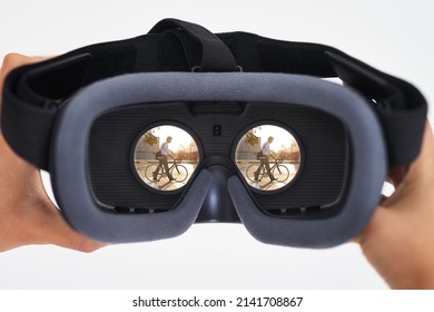 The Age Of Virtual Reality Is Here. Shot Of A Person Holding A VR Headset With A Man Riding A Bicycle Seen In The Lenses.