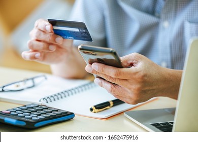 The aged Asian businessman holds a credit card to view online spending.