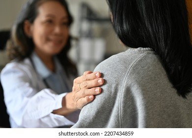 An aged Asian female doctor touching shoulder to comfort and support her patient. A young Asian female patient is being reassured by her doctor. close-up image - Powered by Shutterstock