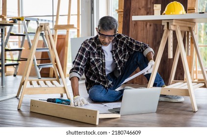 Aged Asian man with blueprint reading data on laptop while making timber furniture in joinery. Older retired people hobby and  DIY in free time  concept. - Powered by Shutterstock