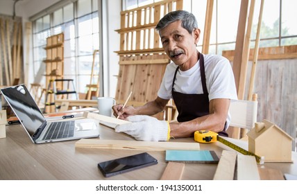 Aged Asian man reading data from laptop and writing in notebook while working in joinery. Home DIY in free time and hobby of older retired people. - Powered by Shutterstock