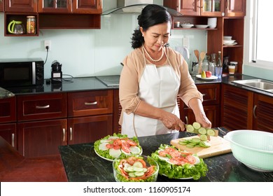 Aged Asian Woman Cooking Salad In Her Kitchen