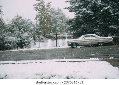 An aged automobile is parked on a snow-covered street next to a fence