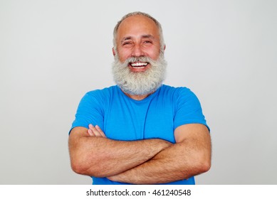 Aged Bearded Fit Man Is Standing With Crossed Hands And Broad Smile Isolated Against White Background