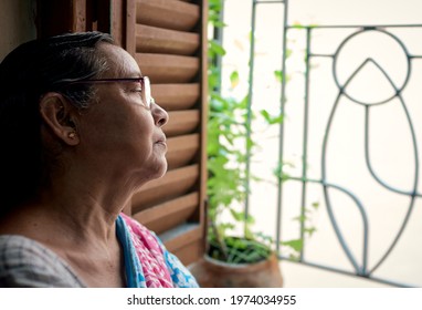 An aged Bengali woman casually staring out of window. There is glimpse of sadness (or anxiety) in her face . Shot taken in Kolkata.