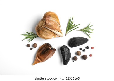 Aged black garlic with rosemary and peppercorns on white background, view from above