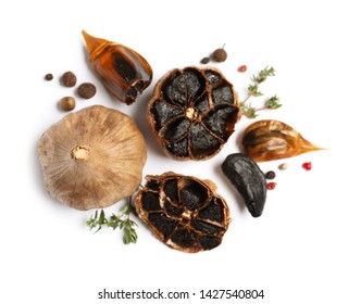 Aged black garlic with thyme and peppercorns on white background, view from above