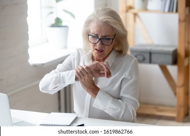 Aged businesswoman sit at workplace desk touch hand feeling wrist pain caused by pc and mouse usage long time wrong arm posture, carpal tunnel syndrome, laptop overwork, joint muscular strain concept