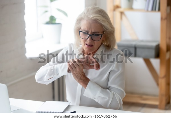 Aged businesswoman sit at workplace desk touch\
hand feeling wrist pain caused by pc and mouse usage long time\
wrong arm posture, carpal tunnel syndrome, laptop overwork, joint\
muscular strain concept