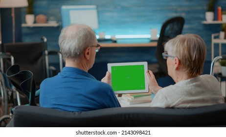 Aged Couple With Chronic Disability Using Green Screen On Digital Tablet. Senior People Looking At Isolated Chroma Key With Blank Mock Up Template And Copy Space Background On Device.