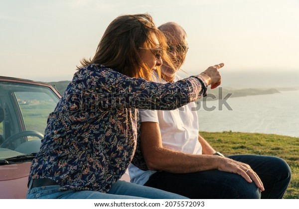 Aged Couple pointing at the\
ocean and traveling through the coast in their 4x4 convertible\
car